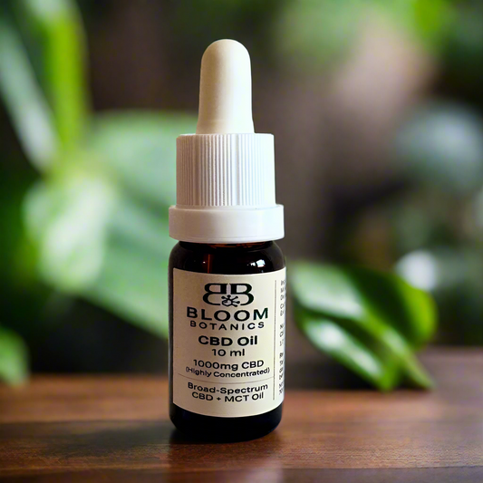 Bottle of Bloom Botanics CBD Oil on a wooden surface with green leaves in the background