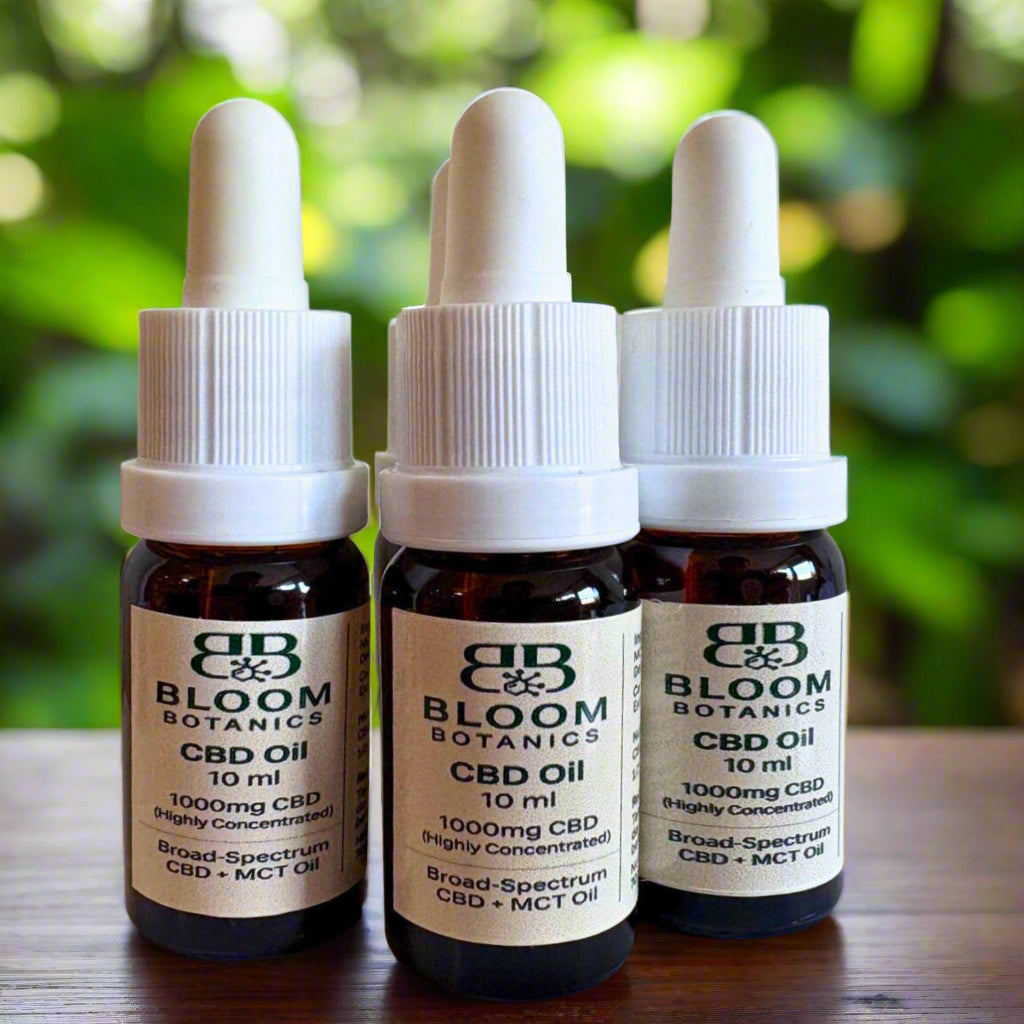 Three bottles of Bloom Botanics CBD Oil on a wooden surface with a blurred green background